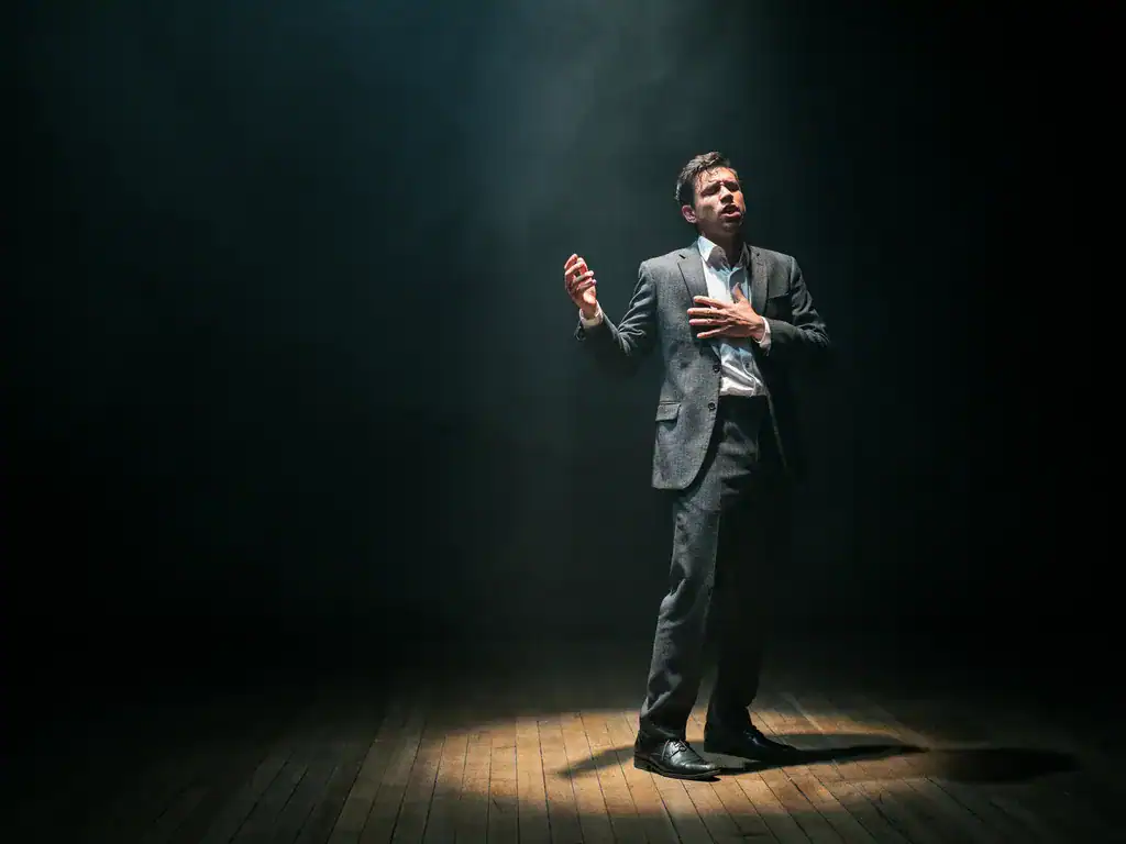 Solo actor performing on stage under a dramatic theatrical spotlight — raw human presence AI cannot replicate